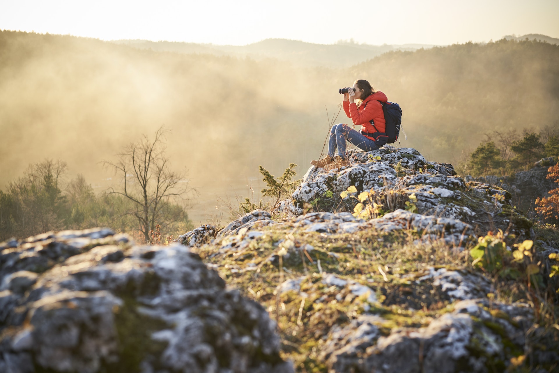Женщина в походе в горах сидит на камне и смотрит в бинокль в Польше