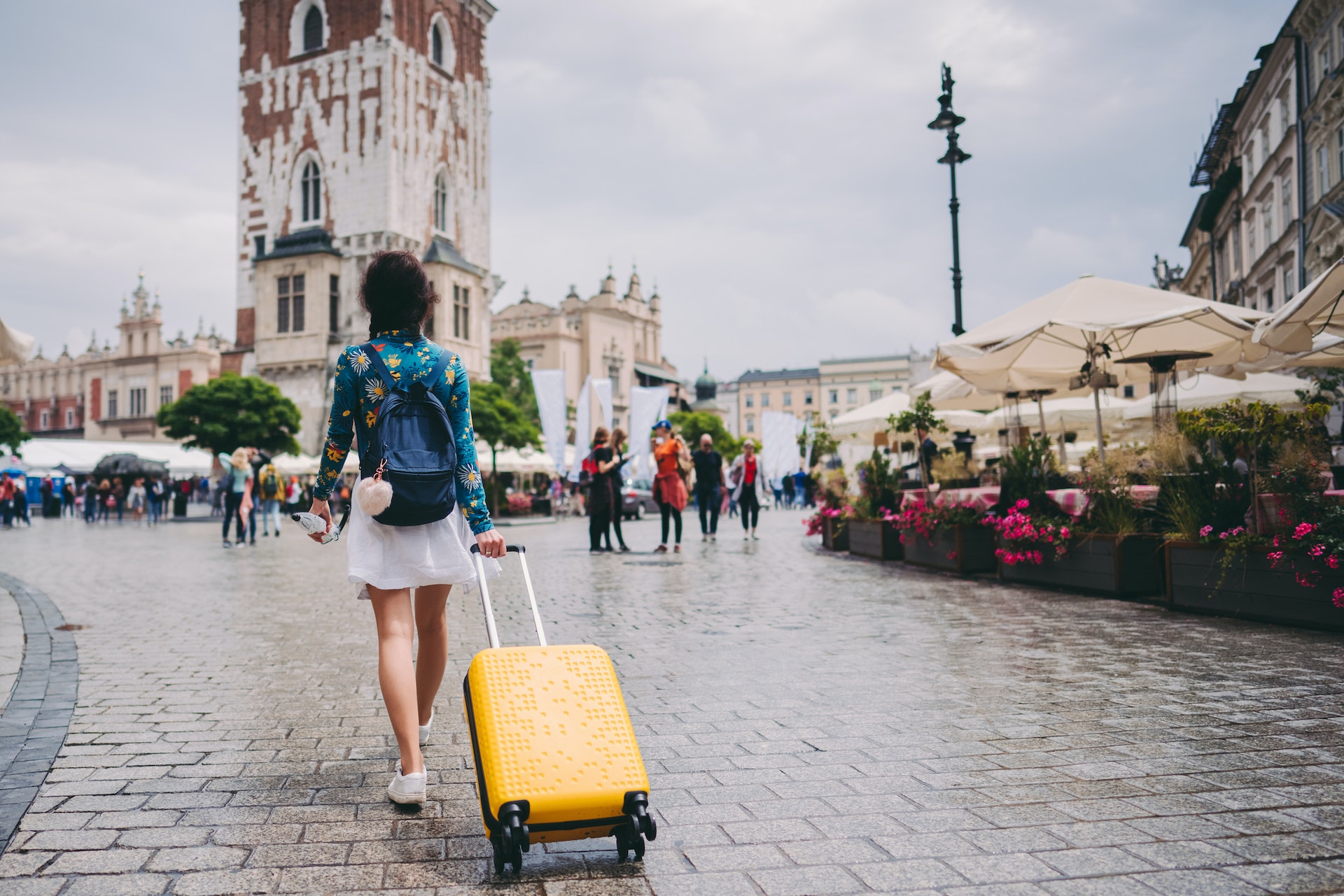 Женщина идет по средневековой площади Кракова с чемоданом.